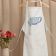apron on hanger with London  tea cup embroidery design behind work table